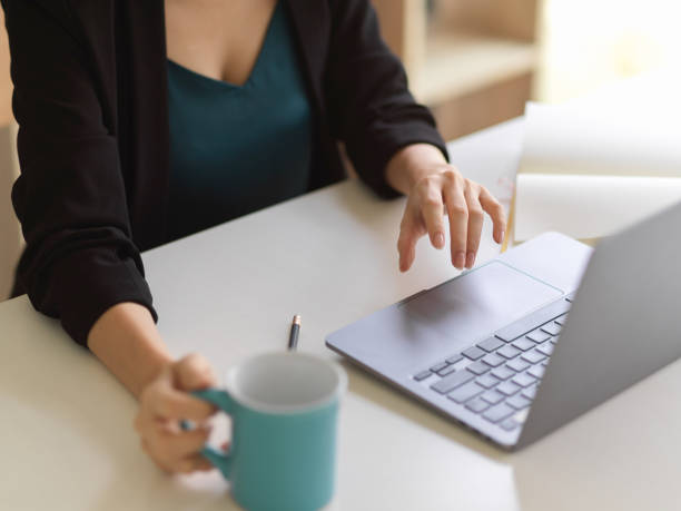 istock Female hand holding coffee cup and working with laptop on office table 1307705614