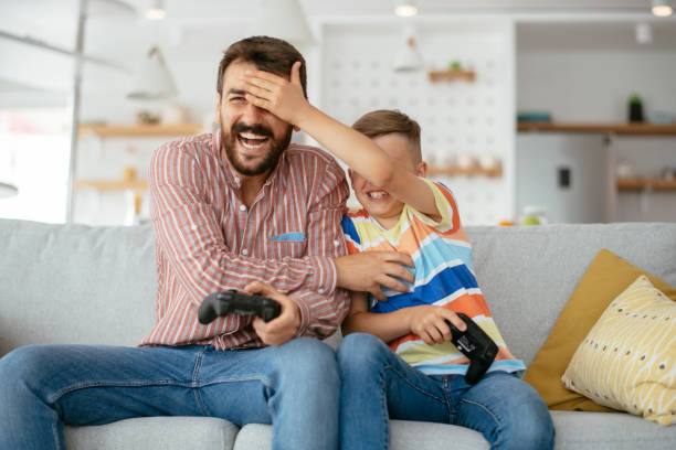 padre e figlio giocano ai videogiochi a casa foto d'archivio - video game family child playful foto e immagini stock