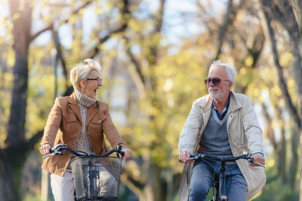 Cheerful active senior couple with bicycle in public park together having fun
