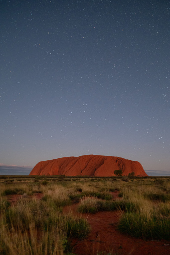 Northern Territory, Australia - March 29, 2016: Night has fallen in the heart of the Australian Outback, and countless stars (and possibly a shooting star) gently illuminates the massive form of Uluru that looms majestically on the horizon.