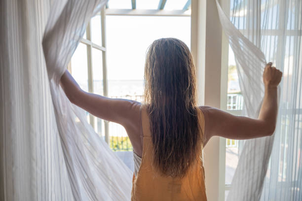 istock Woman opening curtains in room, morning 1307716544