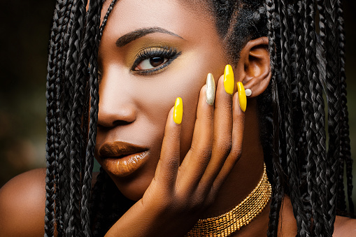 Extreme close up beauty portrait of charming african woman with hand on cheek. Girl with braided hairstyle and sensual look against dark background.