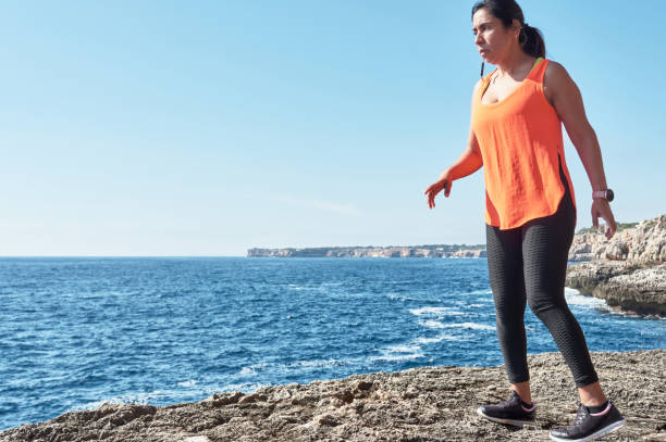 mulher latina, de meia-idade, usando roupas esportivas, treinando, fazendo exercícios físicos, prancha, abdominais, passo do alpinista, queima de calorias, manutenção de forma, ao ar livre à beira-mar, usando fones de ouvido, relógio inteligente - pilates women sit ups yoga - fotografias e filmes do acervo