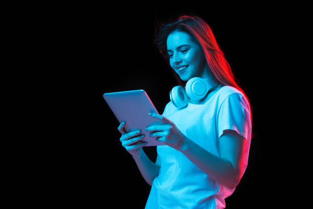 istock Young beautiful girl using device isolated on dark background in neon light 1307721980