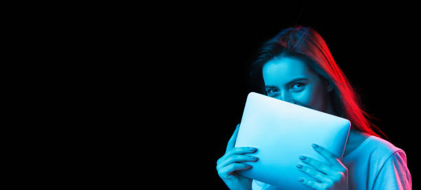 istock Young beautiful girl using device isolated on dark background in neon light 1307721989