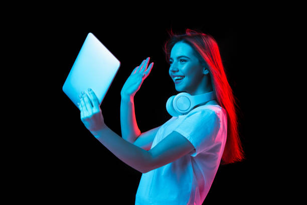 istock Young beautiful girl using device isolated on dark background in neon light 1307721993