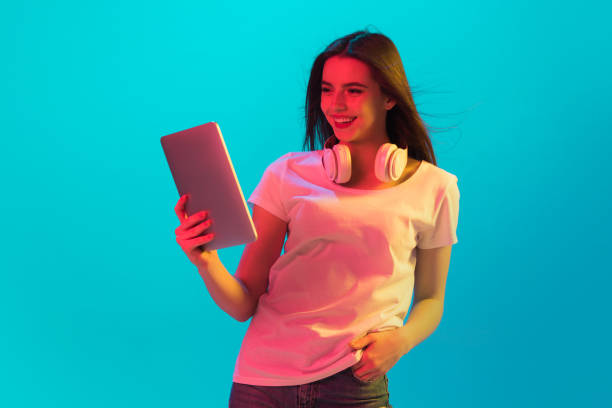 istock Young beautiful girl using device isolated on blue background in neon light 1307722005