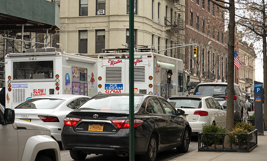 New York, NY, USA - March 17, 2021: Two ice cream trucks find spots near upper east side schools near dismissal time on an early spring day.