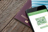 Digital Green Pass concept: Smartphone over a passport and a surgical mask on a wooden table show an hypotetical app for the Digital Green Passport (or digital pass certificate)