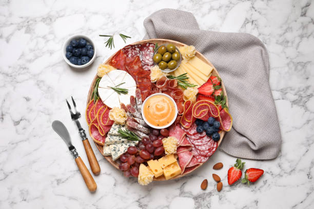 istock Wooden plate with different delicious snacks on white marble table, flat lay 1307726498