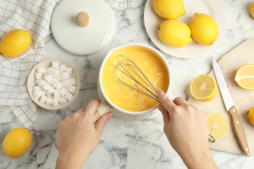 Woman cooking delicious lemon curd at white marble table, top view