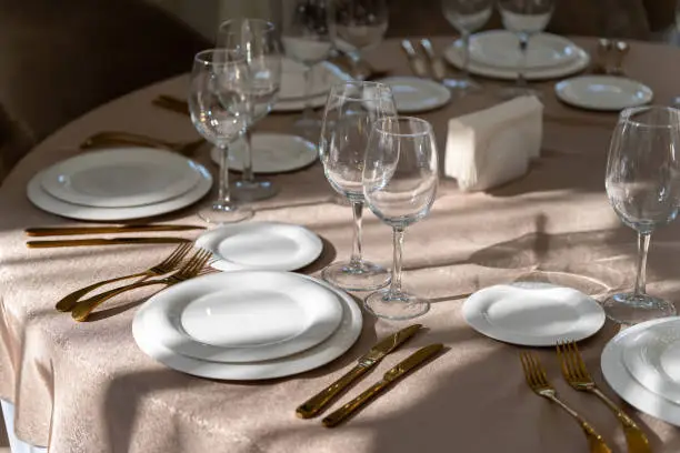 Chic and elegant, gold-plated cutlery and white plates, table setting with empty plates. Luxury restaurant, preparation for the celebration.