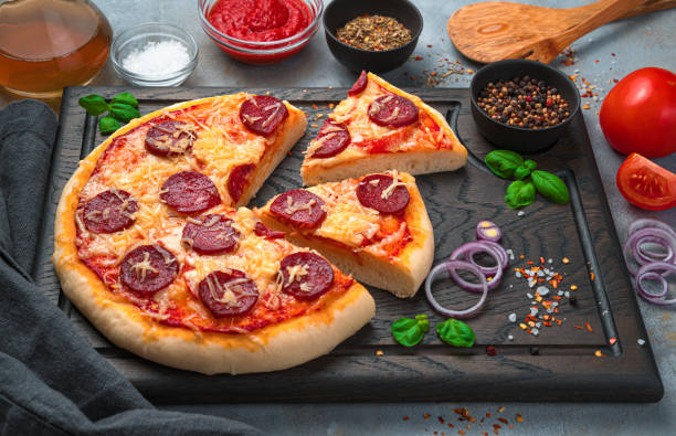 istock Pepperoni pizza on a board with basil, onion and spices on a gray background 1307727006
