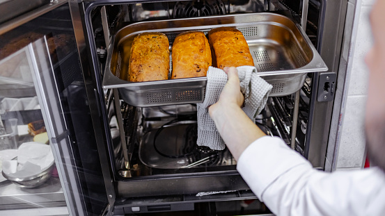 Photo of unrecognizable male baker taking fresh bread out of the oven