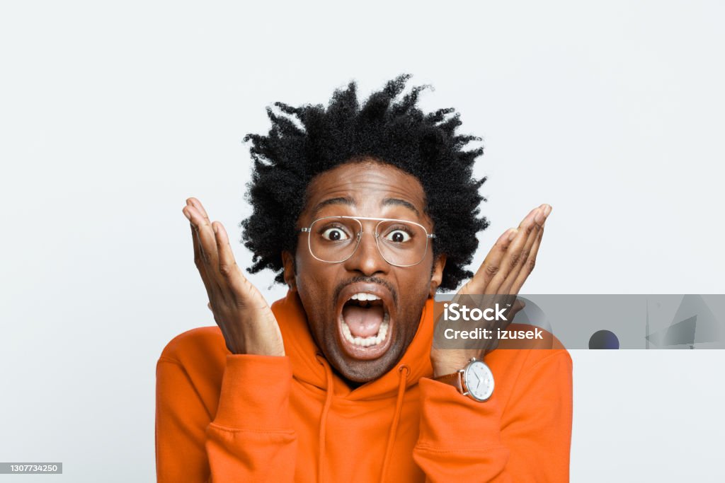Terrified man in orange hoodie Shocked afro american young man wearing orange hoodie and glasses, screaming at camera. Studio shot on grey background. Fear Stock Photo
