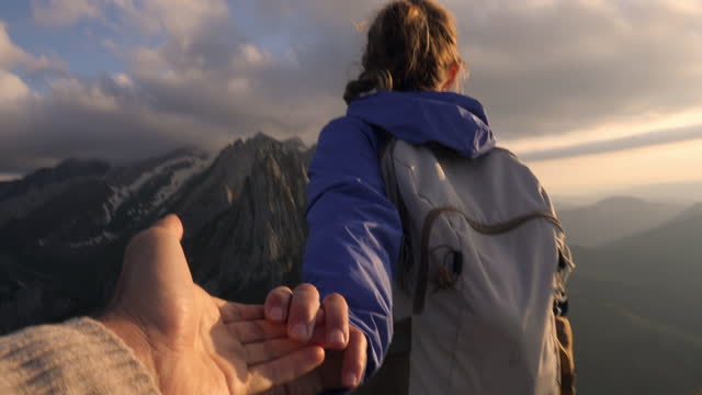 Slow motion: Female hiker holds companion hand and leads him to mountain top.
