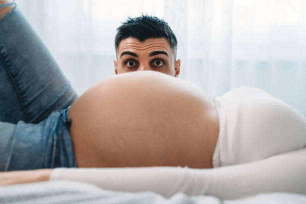tiro engraçado de um homem aparecendo atrás da barriga grávida de sua esposa - human pregnancy pensive women thinking - fotografias e filmes do acervo