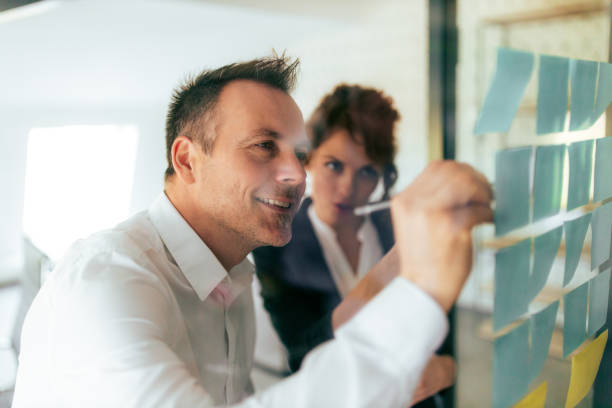 istock Close-up image of a businessman writing on a post it note on glass wall. 1307742702
