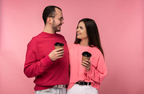 Photo of attractive man wih beard in red clothing and woman in pink holds coffee and gawp on each other. Couple looks happy, isolated over pink background Photo of attractive man wih beard in red clothing and woman in pink holds coffee and gawp on each other. Couple looks happy, isolated over pink background. gawp stock pictures, royalty-free photos & images