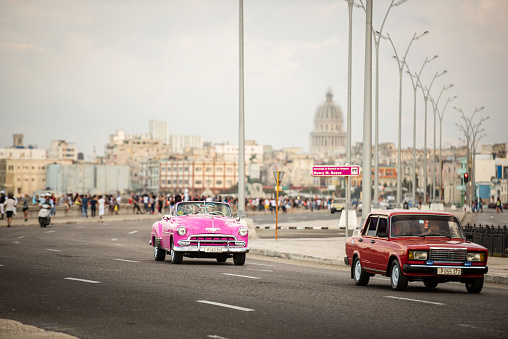 Havana, Cuba - January 22, 2017: A vintage car driving at the Malecon in the evening. In the back you'll find the Capitol and the old city of Havana.