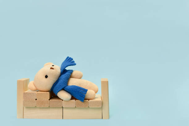A plush toy bear lying in a crib made of wooden cubes. On a light blue background.