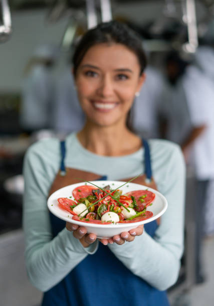 Portrait of a Latin American woman taking cooking lessons and looking very happy presenting a plate - culinary school concepts