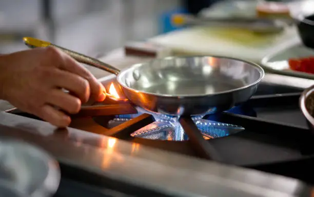 Close-up on a chef lighting up a gas stove burner with a match while working at a restaurant