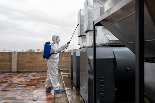 Professional cleaner disinfecting air vents at a factory during the COVID-19 pandemic wearing a protective suit