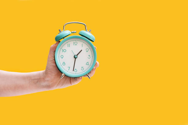 istock Clock. Alarm clock in a female hand on a yellow background. 1307750196
