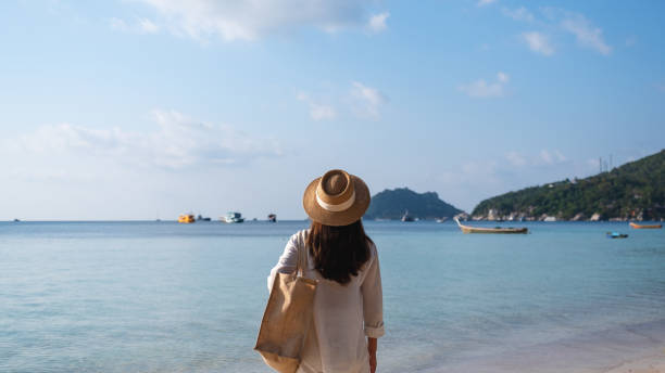 istock a woman with hat and bag strolling on the beach with blue sky background 1307754047