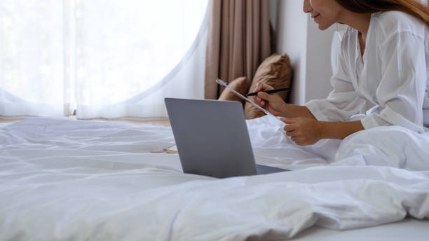istock a beautiful young asian woman using laptop computer and working on paperwork while sitting on bed at home 1307754092
