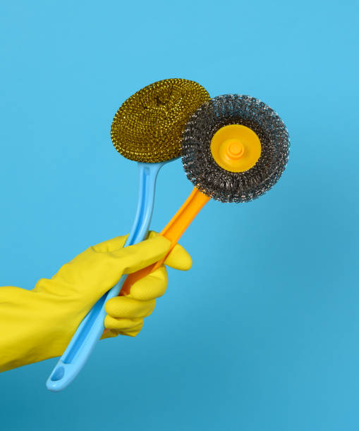 istock hand in a yellow glove holds a stack of plastic cleaning brushes, blue background 1307754213