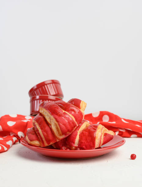 two baked croissants with cherry glaze on a red ceramic plate, white table