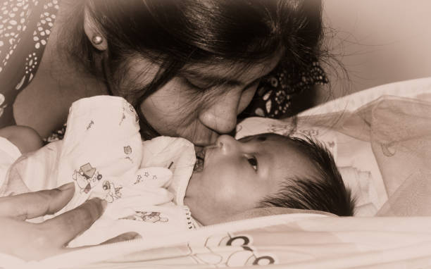 симпатичный новорожденный мальчик поцеловал мать в ее мать коленях, лежащих на кровати. заживать. один месяц старый сладкий маленький млад� - baby holding babies only sign стоковые фото и изображения