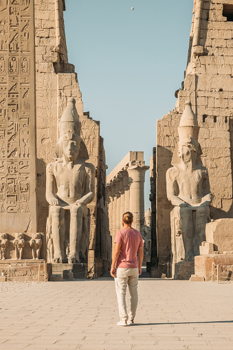 07/03/2023,Luxor,Egypt: An egyptian in traditional clothes standing in front of an obelisk and the entrance of Luxor Temple.Four statues of Ramses can be seen. Luxor Temple is one of the most important tourist attractions in Egypt.