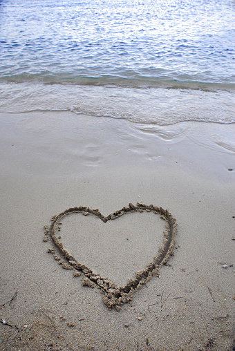 A heart drawn in the sand. Beach background. Top view, space for text.