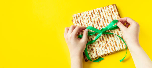 las manos sostienen el pan de matzo sobre un fondo amarillo. feliz pascua. celebración de la fiesta religiosa judía pesach. copiar espacio. - passover matzo bread breaking fotografías e imágenes de stock