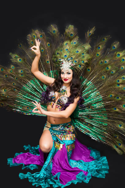 istock Woman in peacock feather carnival costume sitting on floor, isolate black background 1307761022