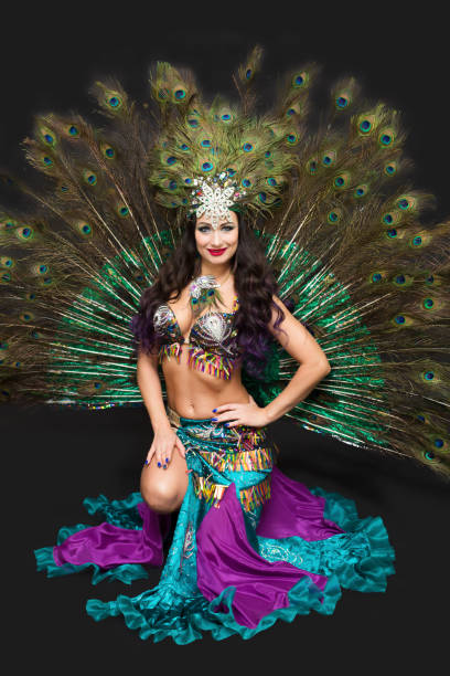istock Woman in peacock feather carnival costume sitting on floor, isolate black background 1307761027