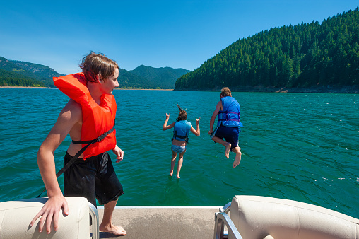 Teenage siblings jump off of boat deck into lake during summer vacation.