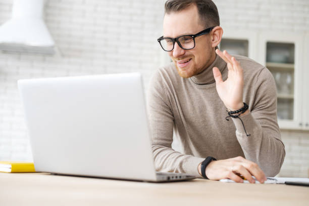 istock Young bearded hipster guy waving at laptop 1307762831