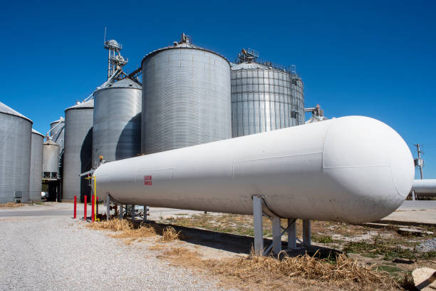 large, long white anhydrous ammonia tank with corn grain bins in background at grain elevator company large, long white anhydrous ammonia tank with corn grain bins in background grain elevator company in countryside. warning decals, stickers, agriculture, food, anhydrous, fertilizer, chemical, plant fertilizer stock pictures, royalty-free photos & images
