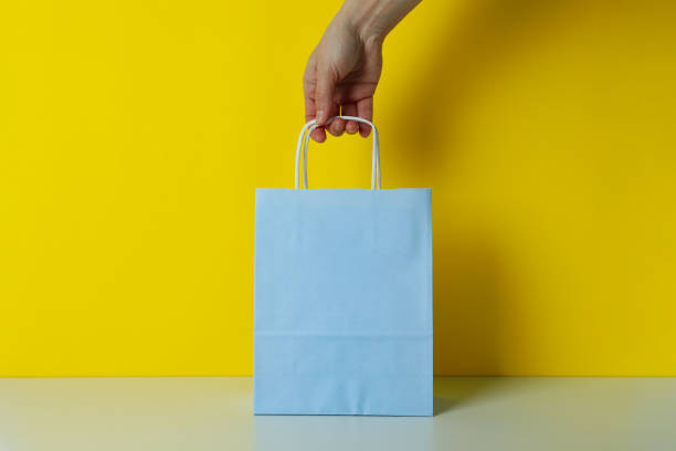 istock Female hand hold paper bag on yellow background 1307770096