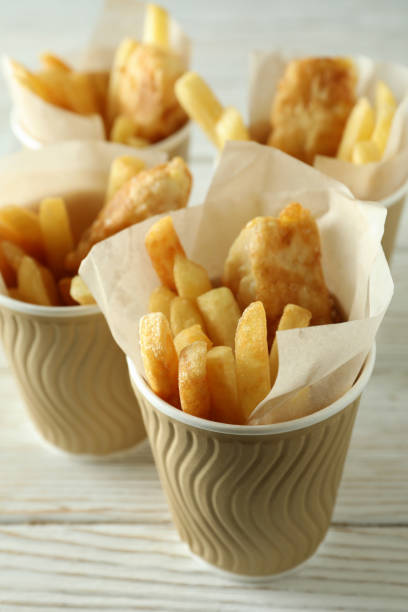 Paper cups with fried fish and chips on wooden background