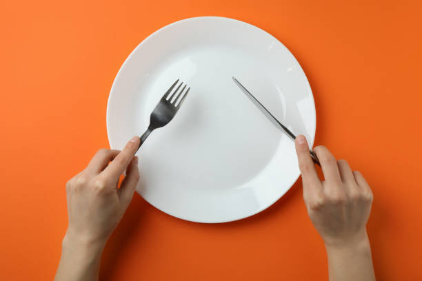 istock Female hands hold cutlery over the empty plate on orange background 1307773265