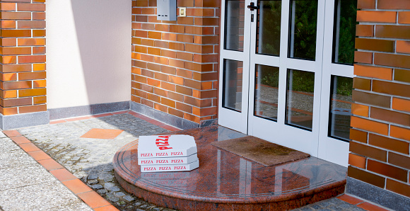 Stack of pizza boxes on the floor in front of door of house during coronavirus pandemic.