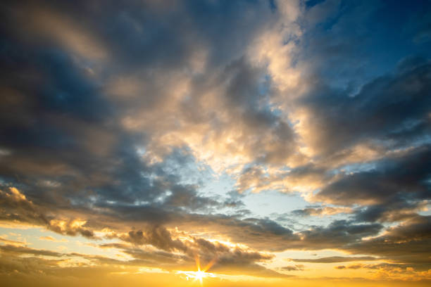 istock Dramatic sunset landscape with puffy clouds lit by orange setting sun and blue sky. 1307774928