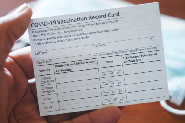 Man Holding COVID-19 Vaccination Record Card A close up of a man holding his blank COVID-19 vaccination card in his hand. Photographed with a very shallow depth of field and a protective face mask out of focus in the background. immunization certificate photos stock pictures, royalty-free photos & images