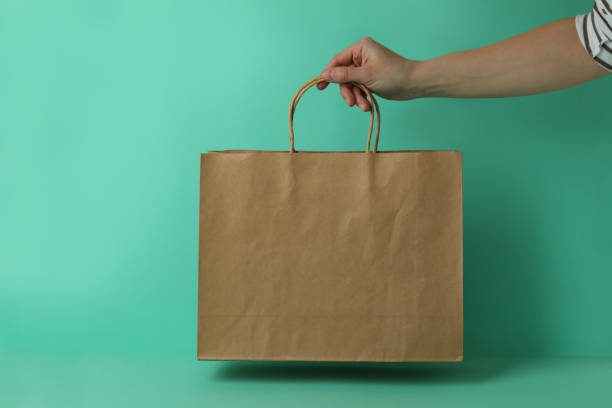 istock Female hand hold paper bag on mint background 1307782618