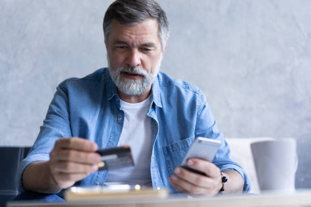 istock Smiling gray-haired 50s man pay bills online using modern smartphone gadget and credit card 1307786445